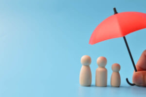 Red toy umbrella and wooden doll figures isolated on a blue background as an insurance coverage concept.